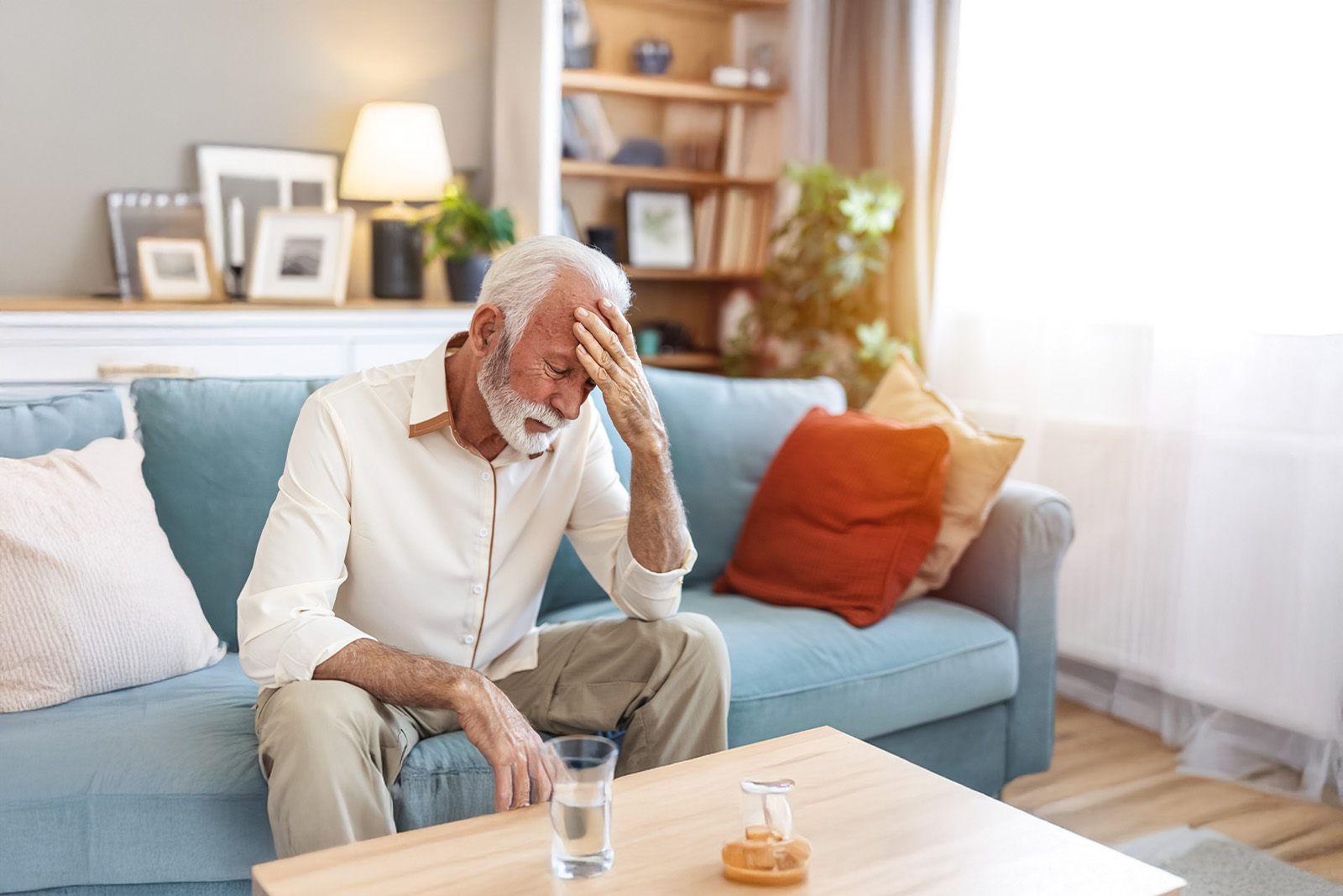 An elderly man sitting on a sofa, looking worried about memory loss.